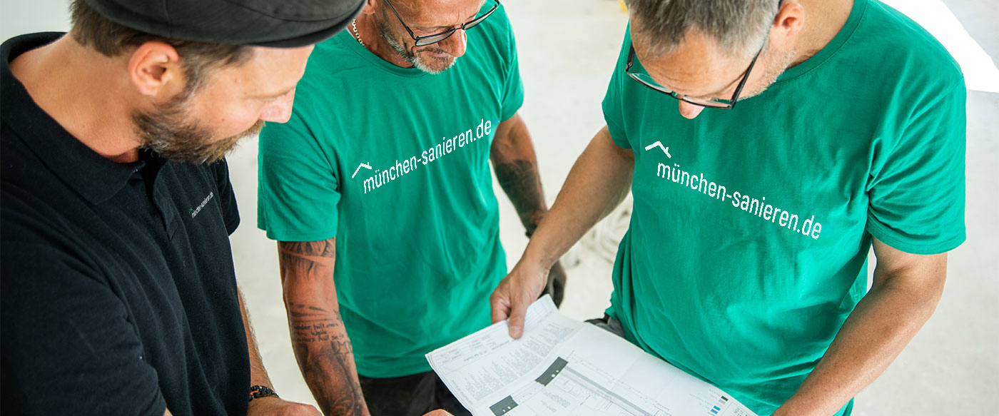 Drei Bauprofis von muenchen-sanieren.de besprechen Baupläne auf einer Baustelle, mit Fokus auf professionelle Sanierungsplanung.