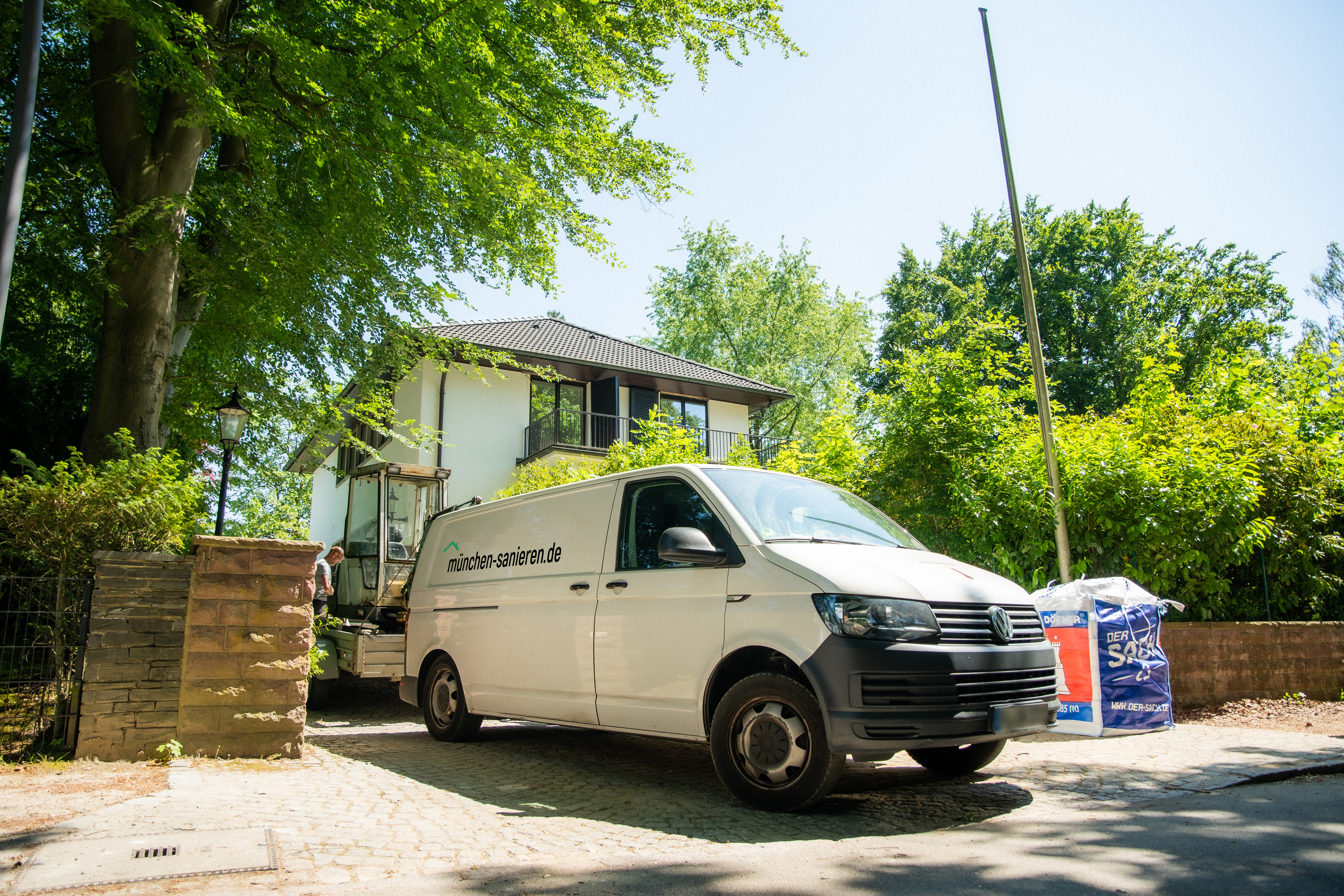 Transporter von hamburg-sanieren.de vor einem Haus, bereit für Sanierungsarbeiten, umgeben von Bäumen und Baustellenmaterial.